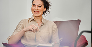 smiling woman sitting in chair holding pen and notebook 
